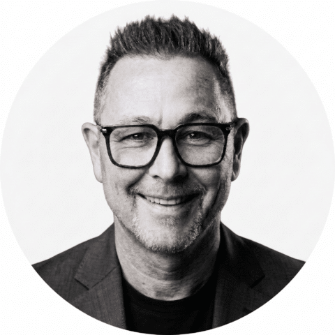 marc-quote Lächelnder Mann mit Brille und kurzen Haaren, der einen Blazer trägt, in einem Schwarz-Weiß-Porträt.